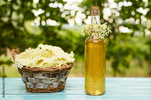 Homemade elderflower syrup in a bottle and basket with flowers of elderflowers