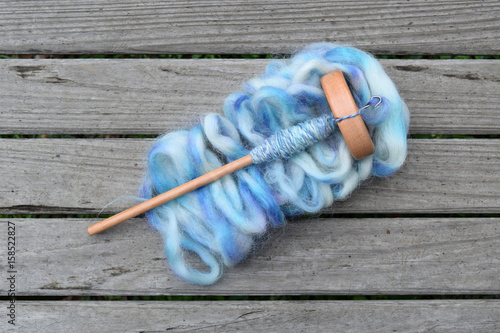 Wood drop spindle with handmade yarn made from the fiber of an alpaca on a wood table on top of a pile of roving