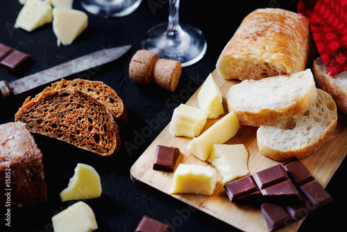 Alcoholic drinks, a holiday, white sparkling wine, glasses with champagne with freshly baked bread, mozzarella cheese and dark chocolate on a black wooden background 