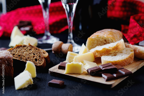 Alcoholic drinks, a holiday, white sparkling wine, glasses with champagne with freshly baked bread, mozzarella cheese and dark chocolate on a black wooden background 