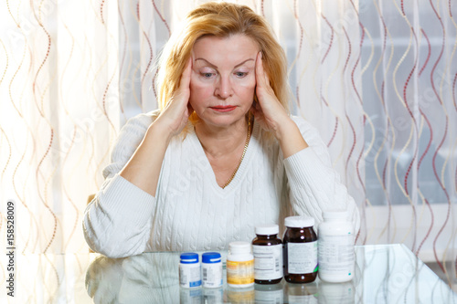 Depressed old senior woman with medicine or health problem. Looking on bottle with pills