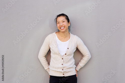 smiling asian woman standing against gray wall