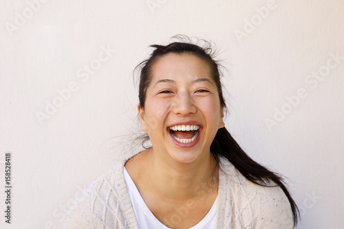 Close up laughing asian woman standing against white wall.