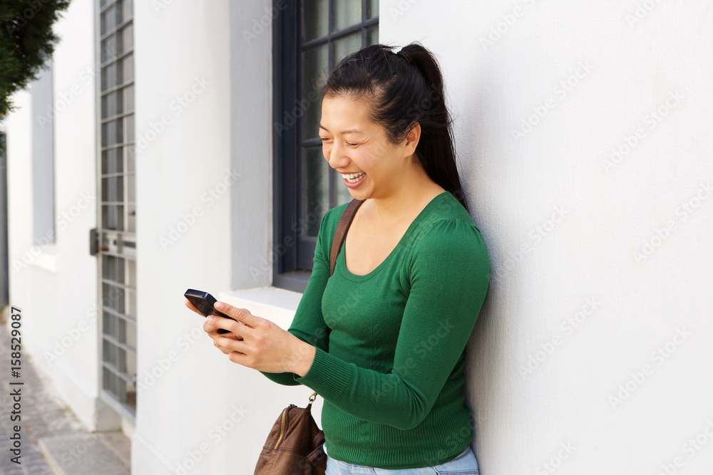 cheerful asian woman standing outside using mobile phone cheerful asian woman standing outside using mobile phone