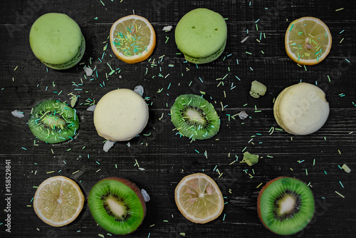 Green and white macaroons with kiwi  orange and lemon in order on a wood gark table