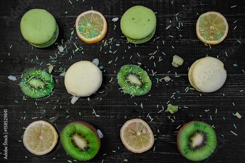 Green and white macaroons with kiwi, orange and lemon in order on a wood gark table photo