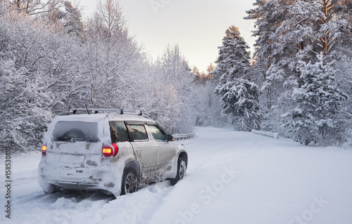 Off-Road Winter Adventure, White SUV Car On Road With Much Snow In Winter Pine Forest. White Crossover Covered With Snow On The Road Among The Winter Forest. Car And Falling Snow In Winter 