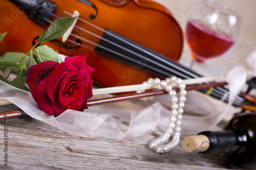 Violin, red rose, pearl necklace and wine on wooden table 