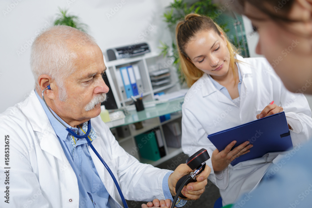 Obraz premium Doctor holding blood pressure gauge, assistant taking notes