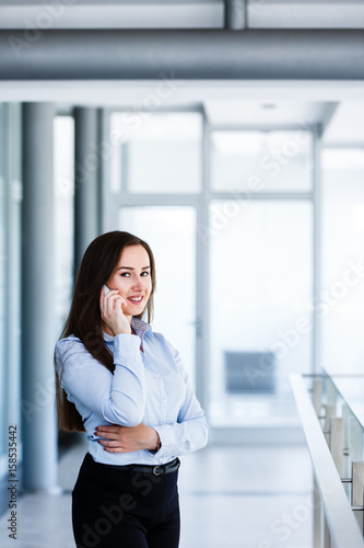 Smiling attractive woman standing in modern interior and talking on phone