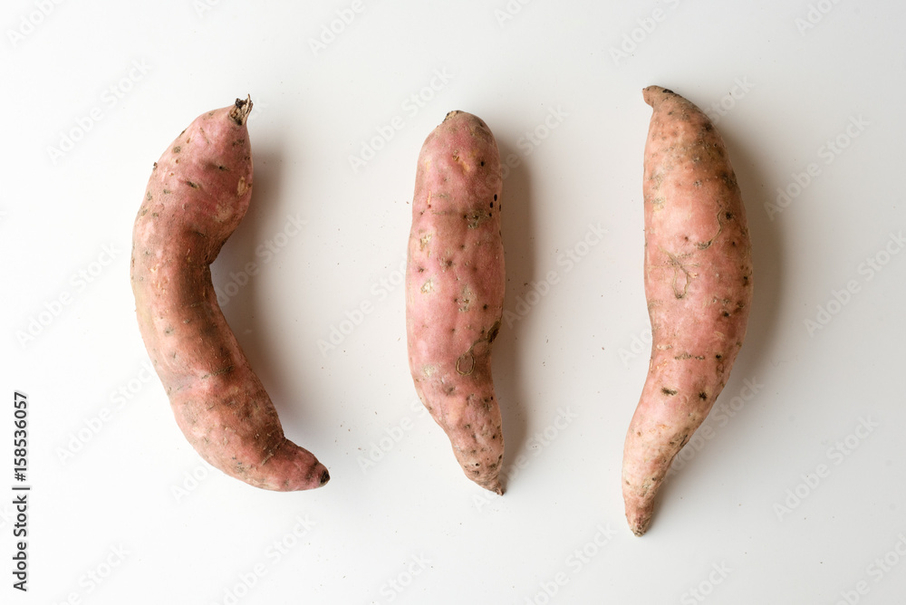 High angle view of three natural looking sweet potatoes on white table High angle view of three natural looking sweet potatoes on white table