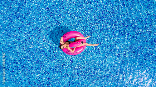 Young girl having fun and laughing and having fun in the pool on an inflatable pink flamingo in a bathing suit in summer from above