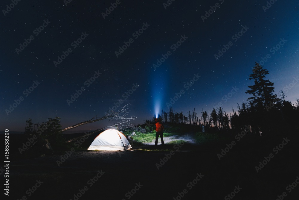 Tourist with flashlight near his camp tent at night