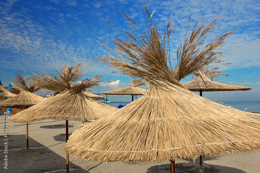 the concept of summer vacation on the beach, straw beach umbrellas at a resort on the ocean