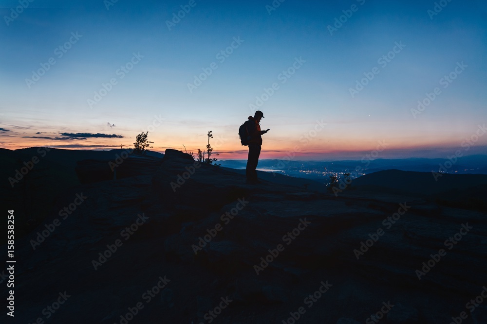 Man tourist standing on top of hill and using his smartphone.