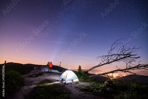Tourist with flashlight near his camp tent at night