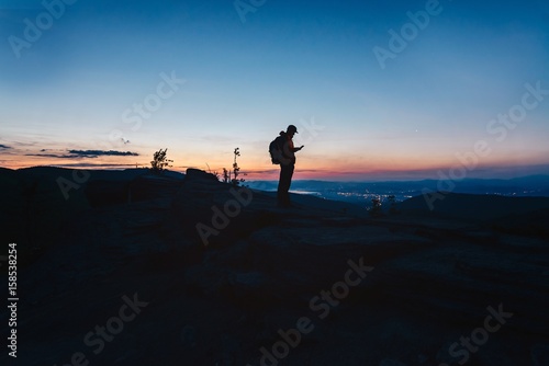 Man tourist standing on top of hill and using his smartphone.