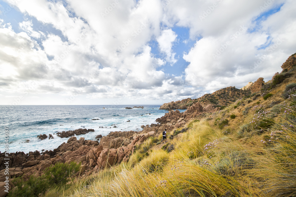 A man with a backpack is hiking along the trail coast of Sardinia in Italy