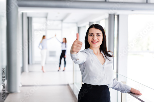 Beautiful modern business woman standing and showing thumbs up while behind are her work colleague