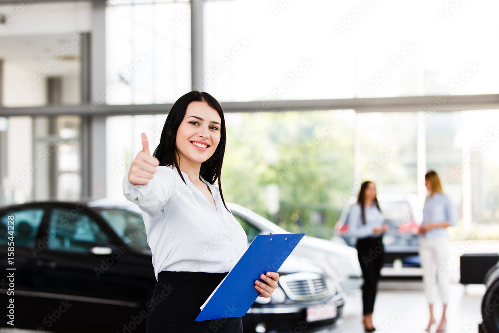 Obraz premium Attractive business woman showing thumbs up while standing in modern car dealership