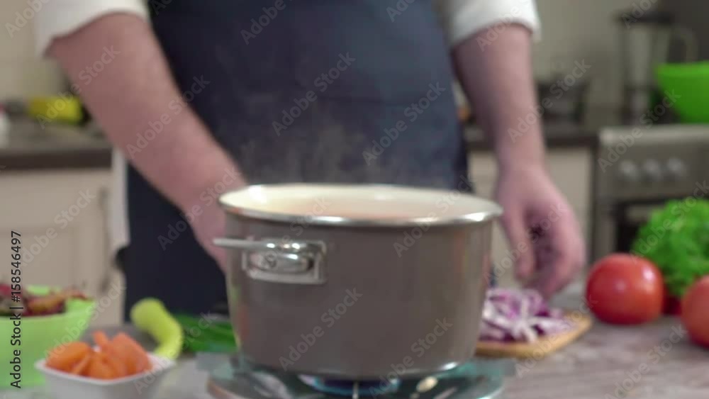 CAUCASIAN CHEF THROWING SLICES OF ONION FROM THE KITCHEN BOARD IN THE COOKING POT, WITH THE KNIFE. RED ONION. GAS BURNER IS ON FIRE, WATER IS BOILING. HORIZONTAL DOLLY SHOT CAUCASIAN CHEF THROWING SLICES OF ONION FROM THE KITCHEN BOARD IN THE COOKING POT, WITH THE KNIFE. RED ONION. GAS BURNER IS ON FIRE, WATER IS BOILING. HORIZONTAL DOLLY SHOT