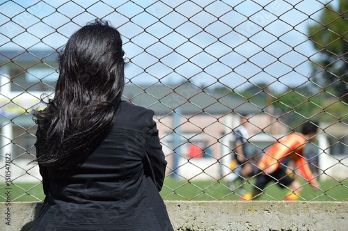 Young mother encourages her son soccer player from the edge of the playing field