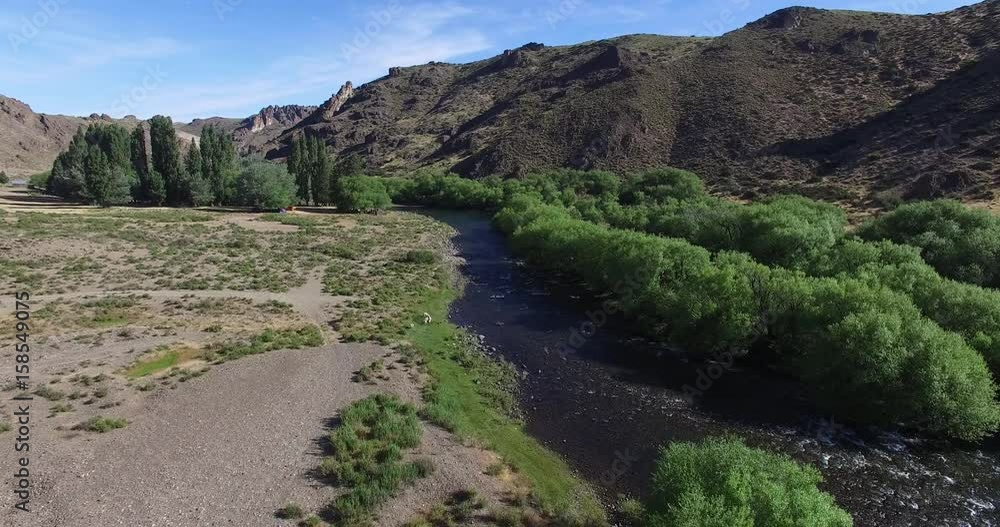 Aerial drone scene of gravel route with a people in van fly fishing river in a steppe scenario in south Patagonia, Argentina. Camera moving forward on a side of the road. People playing in the water.