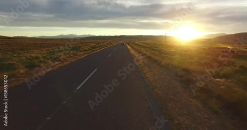 Aerial drone scene of route in steppe landscape at sunset golden hour. Camera moving forward following a tracked van on the road.