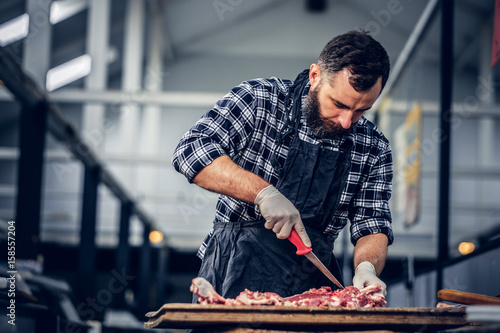 фотографія Bearded butcher cut fresh bacon meat.