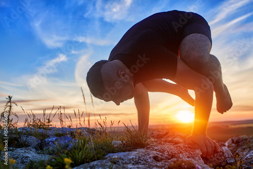 Attractive man doing yoga on the rock in the morning against sunrise.