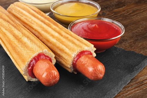 French hot dog and bowls with sauces on a slate board. Fast food.