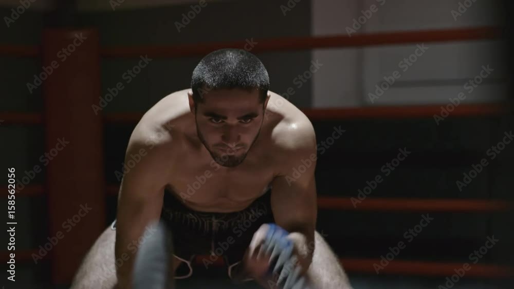 Shirtless tough sportsman with big muscles working out with rope in dark gym Shirtless tough sportsman with big muscles working out with rope in dark gym