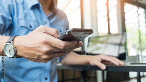 Smiling young casual business man with mobile phone in the hand in office