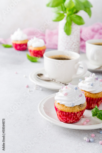 Mini cupcakes with white frosting cream and pink sprinkles on light gray background. Decorated with basil leaves. Party food concept. Copy space.