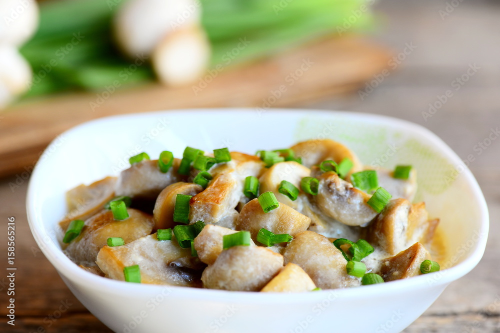Mushrooms slices in a sour cream sauce. Mushrooms stewed with sour cream and green onions in a bowl. Healthy vegetarian snack recipe. Vintage wooden table. Closeup Mushrooms slices in a sour cream sauce. Mushrooms stewed with sour cream and green onions in a bowl. Healthy vegetarian snack recipe. Vintage wooden table. Closeup