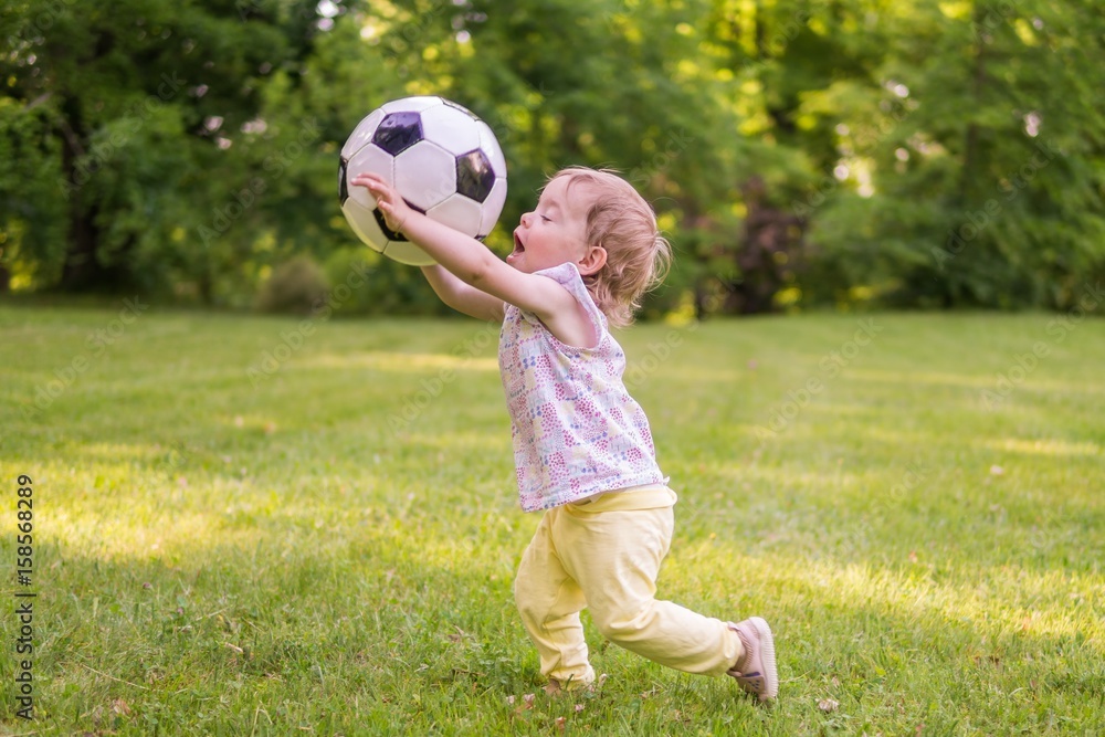 Obraz premium Little child is playing with football ball in park.