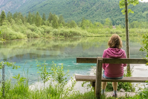 Woman is sitting on bench near lake in Austria near Alps. © vchalup