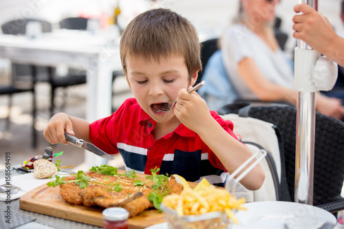 Preschool child  eating big steak of meat and french fries