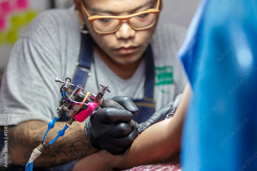 Close up tattoo artist demonstrates the process of getting black tattoo with paint. Master works in black sterile gloves.