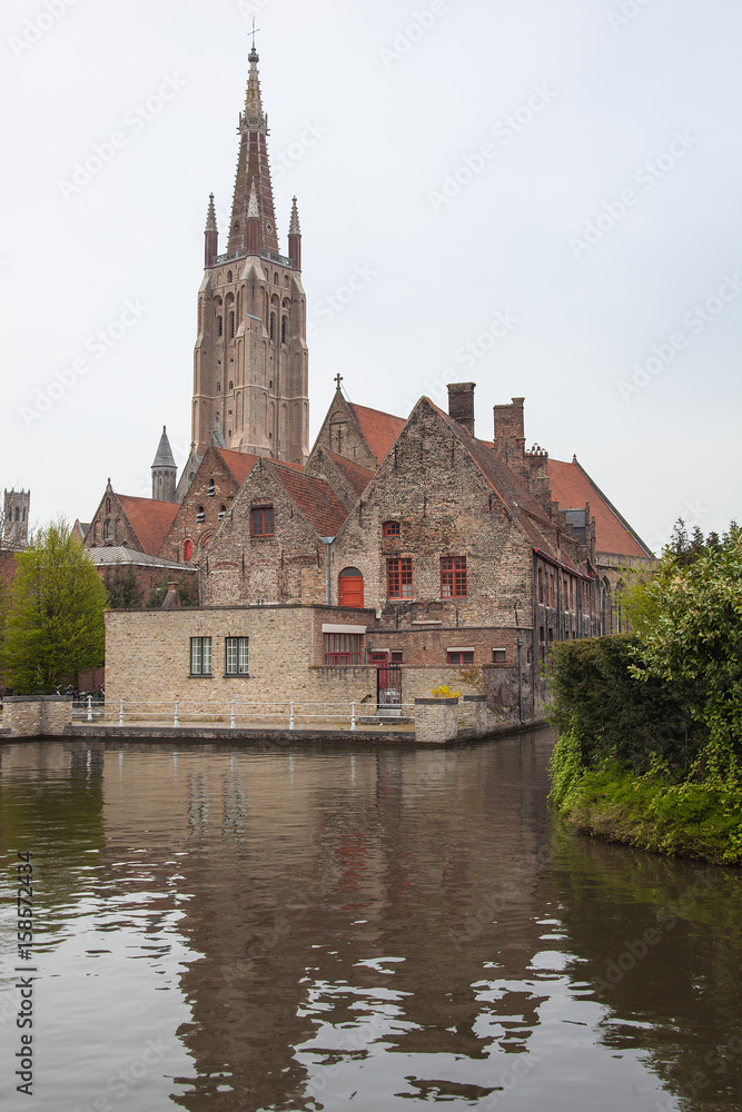 Fototapeta premium View of Minnewater pond with historical red brick buildings and the tower of the Church of Our Lady in spring in the medieval neighborhood of Bruges (Brugge), Belgium
