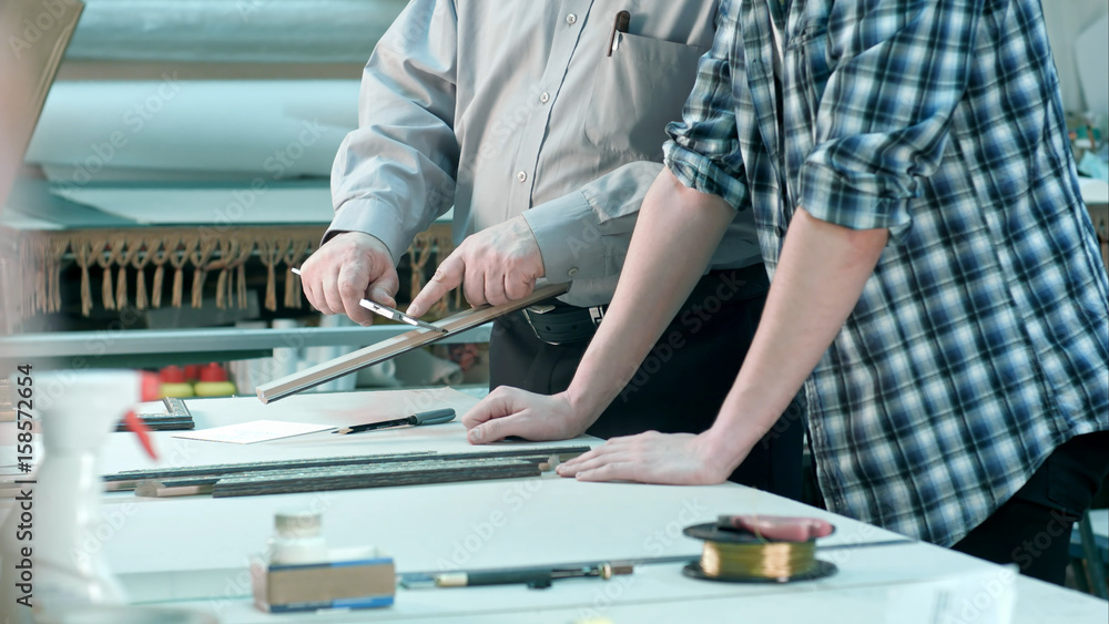 Male workers measuring size of frame behind the desk in workshop Male workers measuring size of frame behind the desk in workshop
