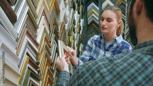 Male worker chatting with customer about picture frame details in atelier