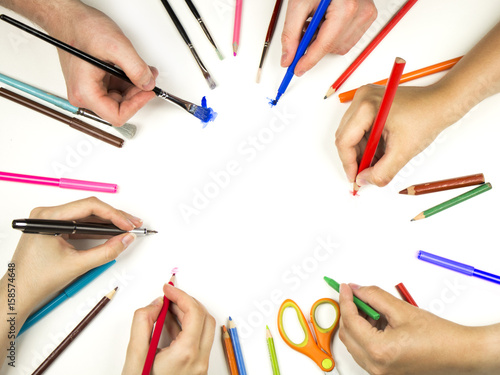 Photo of many hands holding art supplies - top view