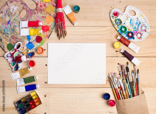 Paints, brushes and palette on the white wood background. The workplace of the artist. Banner for school