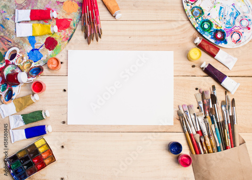 Paints, brushes and palette on the white wood background. The workplace of the artist. Banner for school