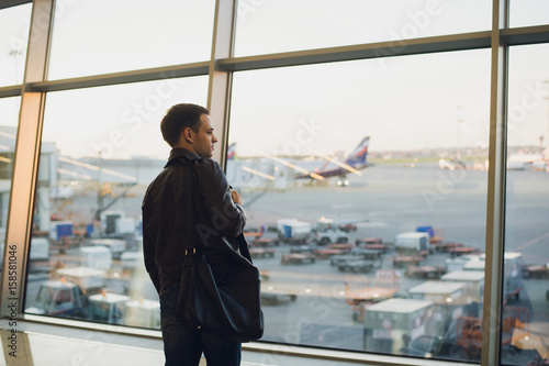 Travel concept with young man in airport interior with city view and a plane flying by.