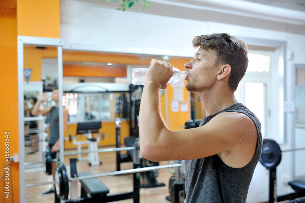 Fototapeta premium Young athlete drinks a cool drink in the gym