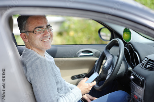 Smiling man in a car with smartphone in the hand