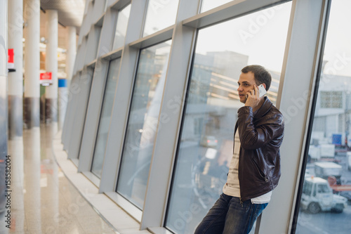 Traveler inside airport terminal. Young man using mobile phone and waiting for his flight. © romankosolapov