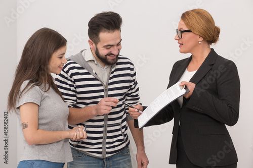 Fototapeta Naklejka Na Ścianę i Meble -  Estate agent pointing to a place in purchase agreement where new owners have to put a signature. Realtor showing agreement to a happy couple.